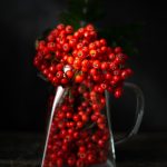 a glass vase filled with red berries on top of a table